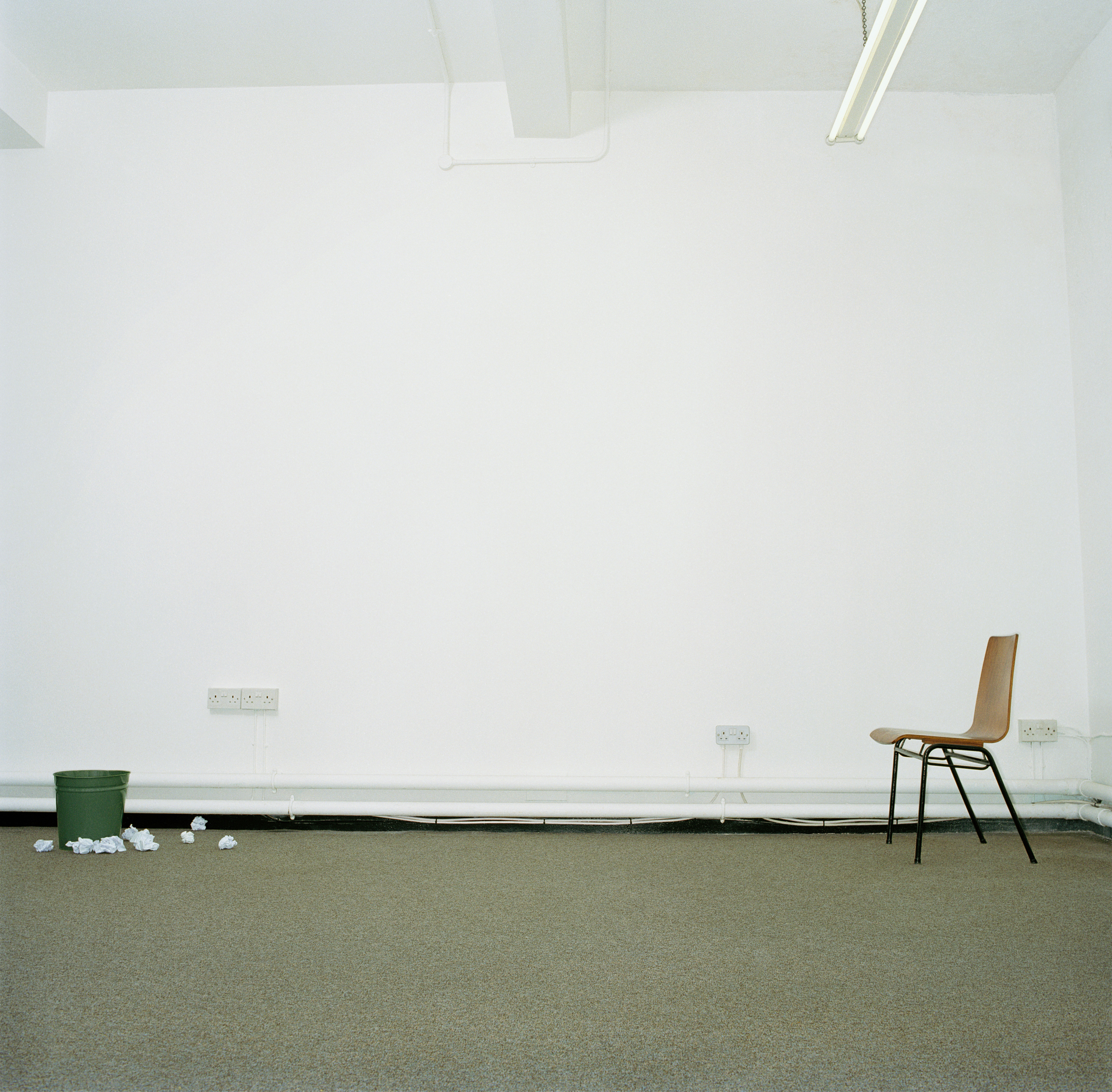 Image of a chair and a trash can in an office, with the bin surrounded by crumpled paper, representing persistence.