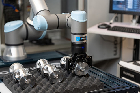 Robotiq 2F-85 cobot gripper picking a finished part with an encompassing grip.