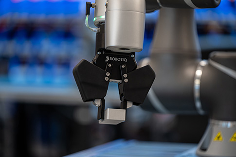 Robotiq 2F-85 cobot gripper picking a raw part with a parallel grip.