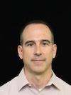 Professional headshot of a man with light brown hair against black background